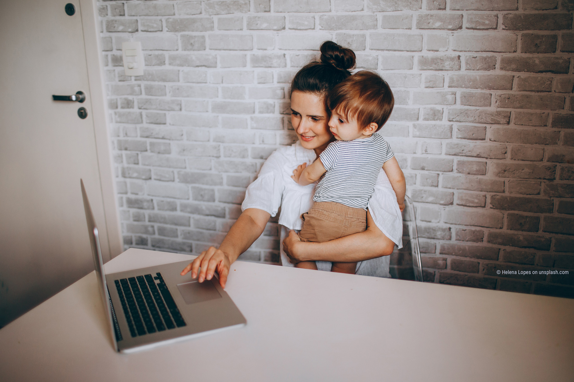 Frau mit Kleinkind im Arm arbeitet mit der anderen Hand am Laptop